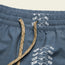Close-up of blue boardshorts featuring a beige drawstring, an elastic waistband, and a repeating white seagull pattern along the waistband and side seam. 7” inseam offers comfort and style for any beach day.