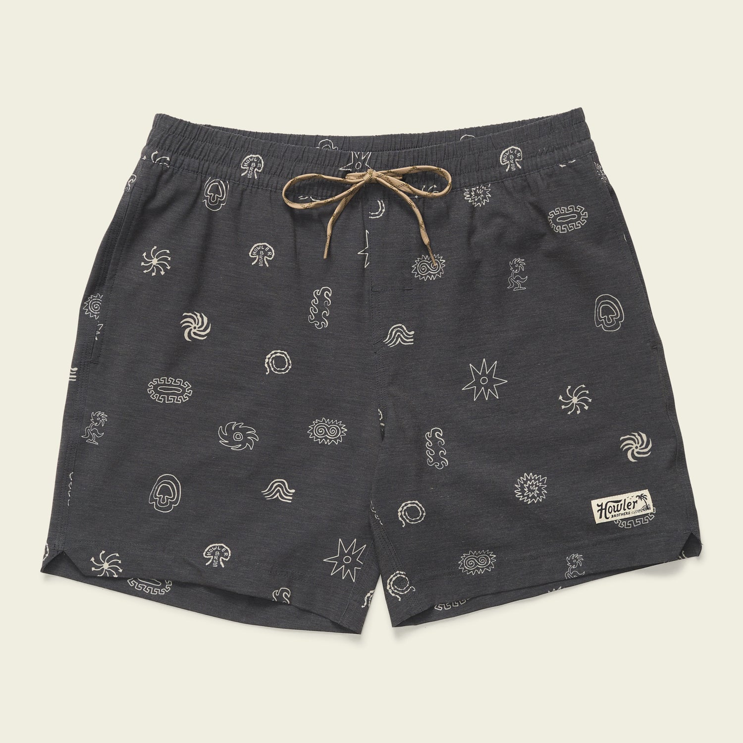 Dark gray boardshorts featuring a 7” inseam, tan drawstring, and small white abstract patterns throughout. An elastic waistband ensures comfort, while a rectangular patch with “Howler” is sewn near the lower left hem.