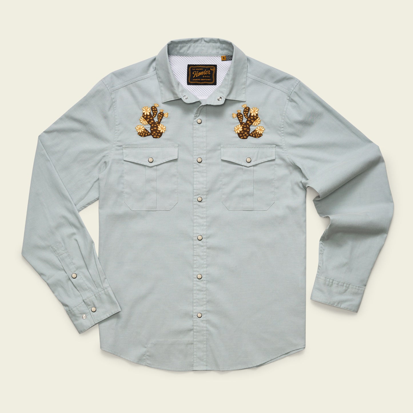 A light blue Gaucho Snapshirt, this long-sleeve button-up features two front pockets and embroidered brown and gold cactus designs, echoing the charm of vintage western shirts.