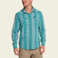 A man wearing a teal and white plaid lightweight stretch shirt with two chest pockets and khaki pants, standing and smiling against a light background.