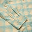 A close-up of a light blue and beige plaid Matagorda Shirt sleeve, showing the cuff with white buttons and detailed stitching. This travel shirt features a soft, checkered pattern and quick drying fabric for comfort on the go.