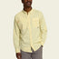 A man wearing a light yellow, long-sleeve Matagorda Shirt with a small checkered pattern and two chest pockets, standing with one hand in his gray pants pocket against a plain background. This travel shirt is quick drying and stylish.