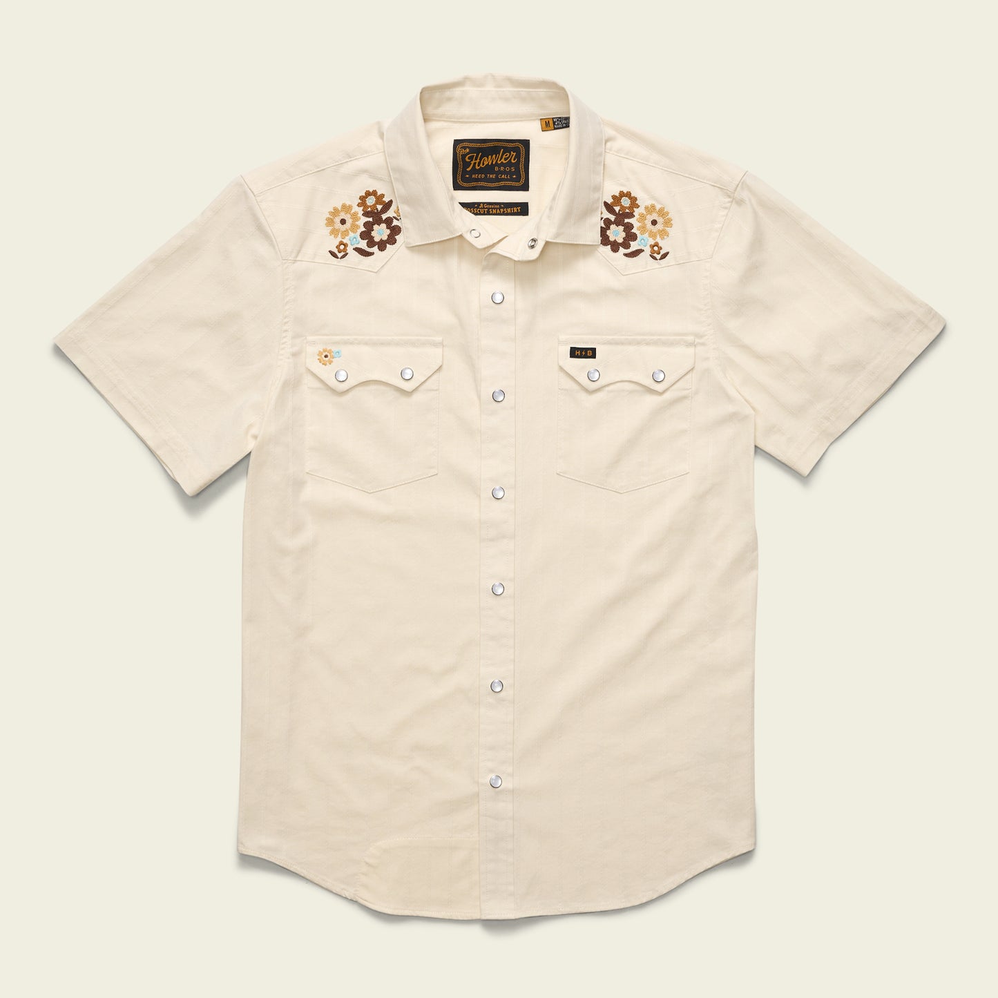 Short-sleeve, cream-colored Crosscut Deluxe Shortsleeve western shirt with white snap buttons, two front pockets, and floral motif embroidery in brown, yellow, and cream above the chest—a perfect summer shirt.