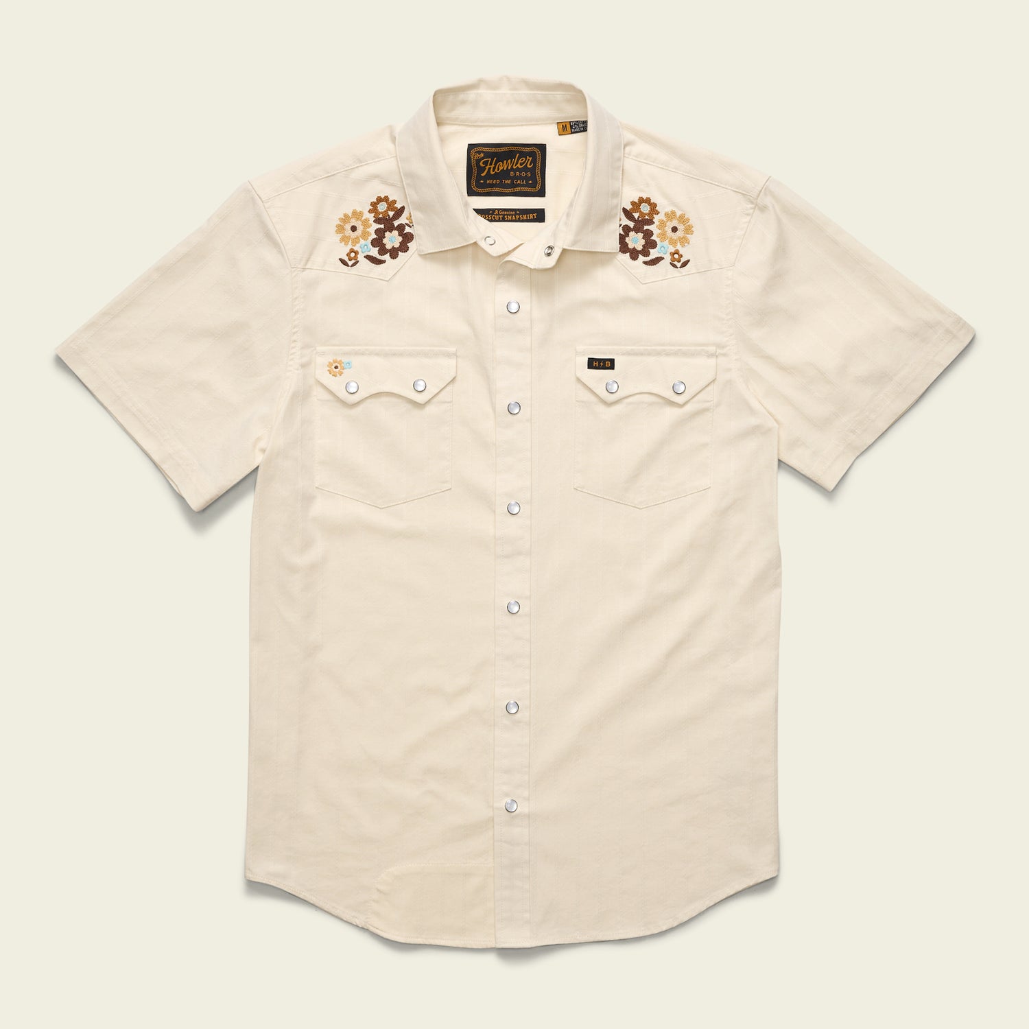 Short-sleeve, cream-colored Crosscut Deluxe Shortsleeve western shirt with white snap buttons, two front pockets, and floral motif embroidery in brown, yellow, and cream above the chest—a perfect summer shirt.