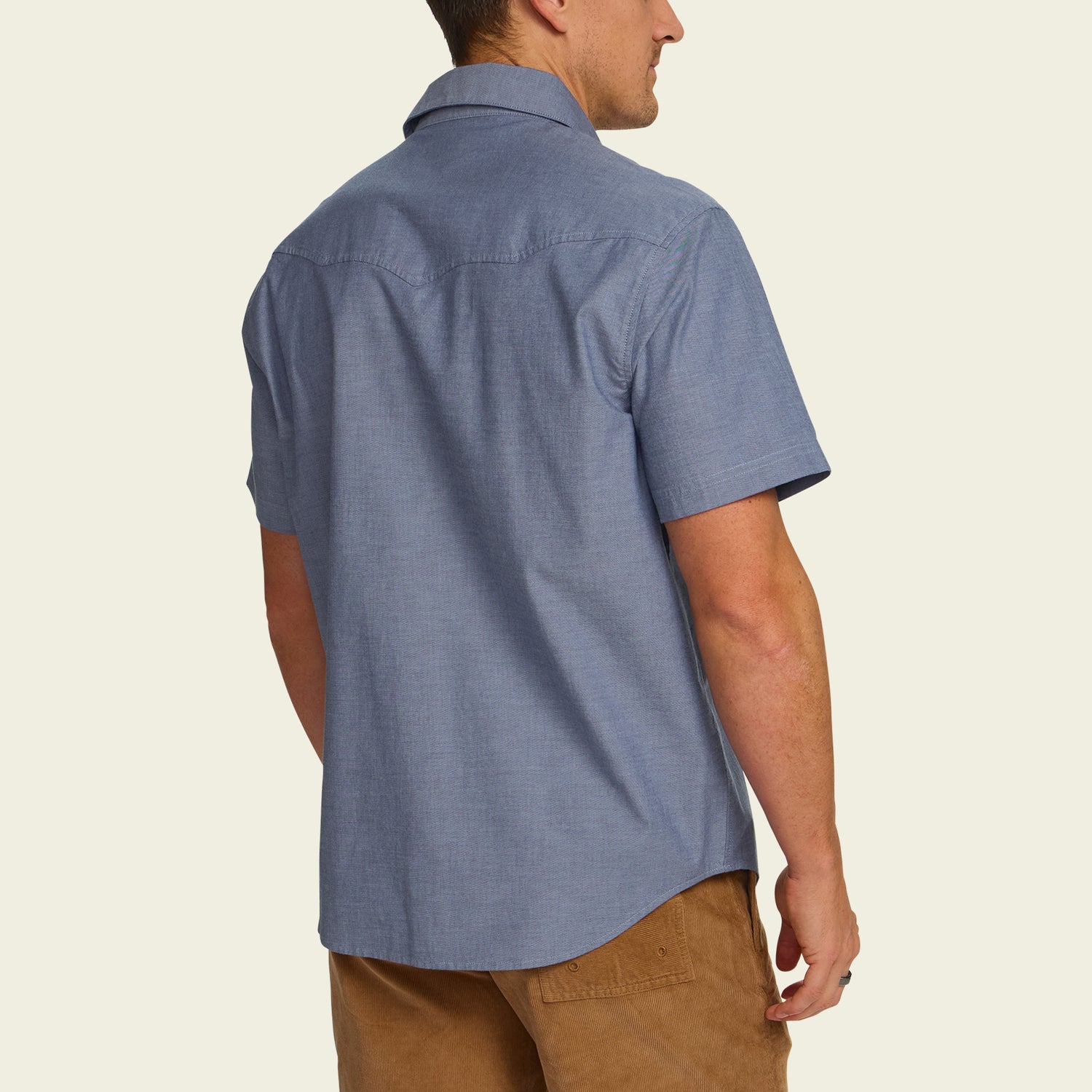 A man is shown from behind wearing a light blue Crosscut Deluxe Shortsleeve summer shirt and tan pants, standing against a plain light background.