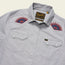 A light gray Crosscut Deluxe Shortsleeve summer shirt with pearl snap buttons, two chest pockets, and red and blue motif embroidery of eye designs on both shoulders. The label reads Howler and indicates size Medium.