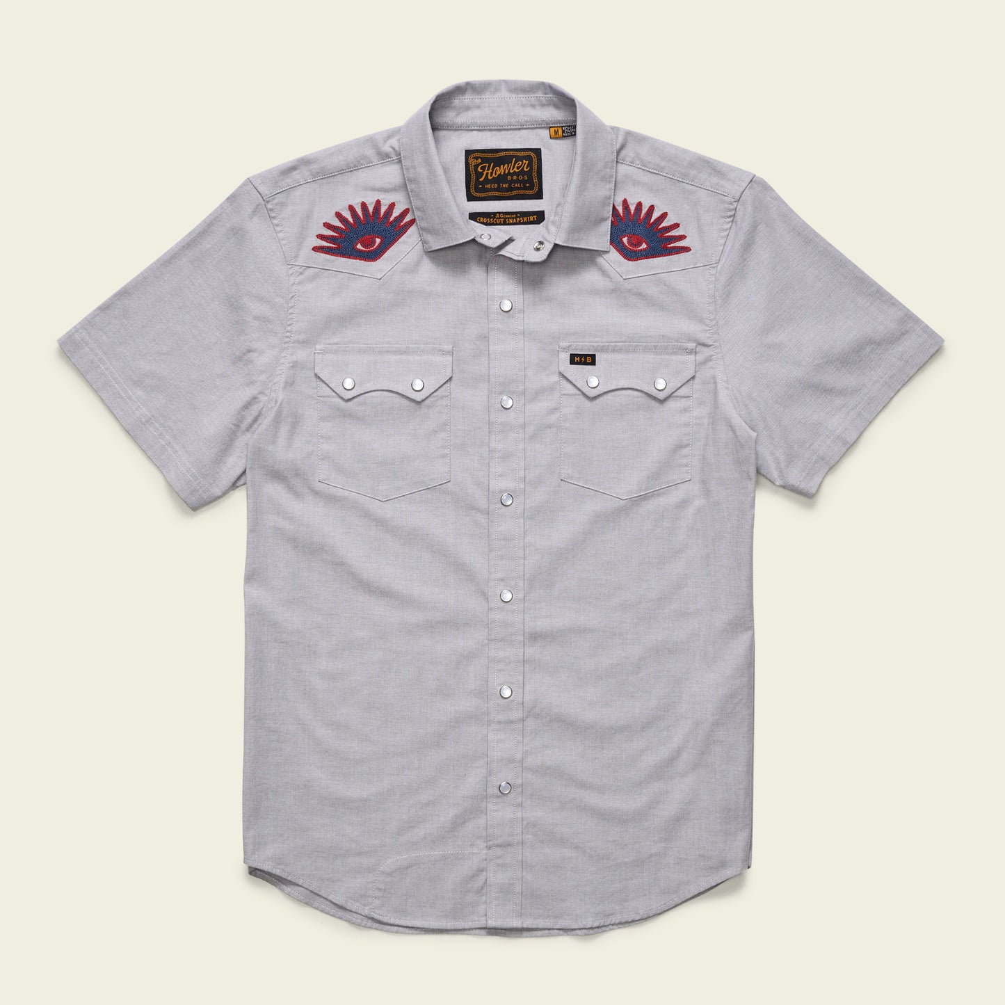 A light gray Crosscut Deluxe Shortsleeve summer shirt with two chest pockets and red motif embroidery of eye designs above each pocket on the upper chest area.