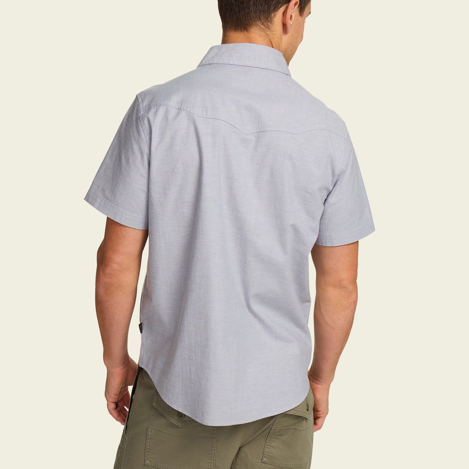 A man is shown from the back wearing a light blue Crosscut Deluxe Shortsleeve summer shirt and olive green pants against a plain, light background.