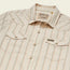 A vintage inspired shirt from Howler Brothers, this beige short-sleeve button-up features light blue and orange diagonal stripes, two front flap pockets, brown snap buttons, and a “Howler” label above the left pocket.