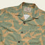 A beige short-sleeve button-up Monoloha Shirt with a green tropical leaf pattern and dark buttons, laid flat to display the collar and chest pocket. The tag reads Howler Brothers, channeling classic vintage Hawaiian shirts style.