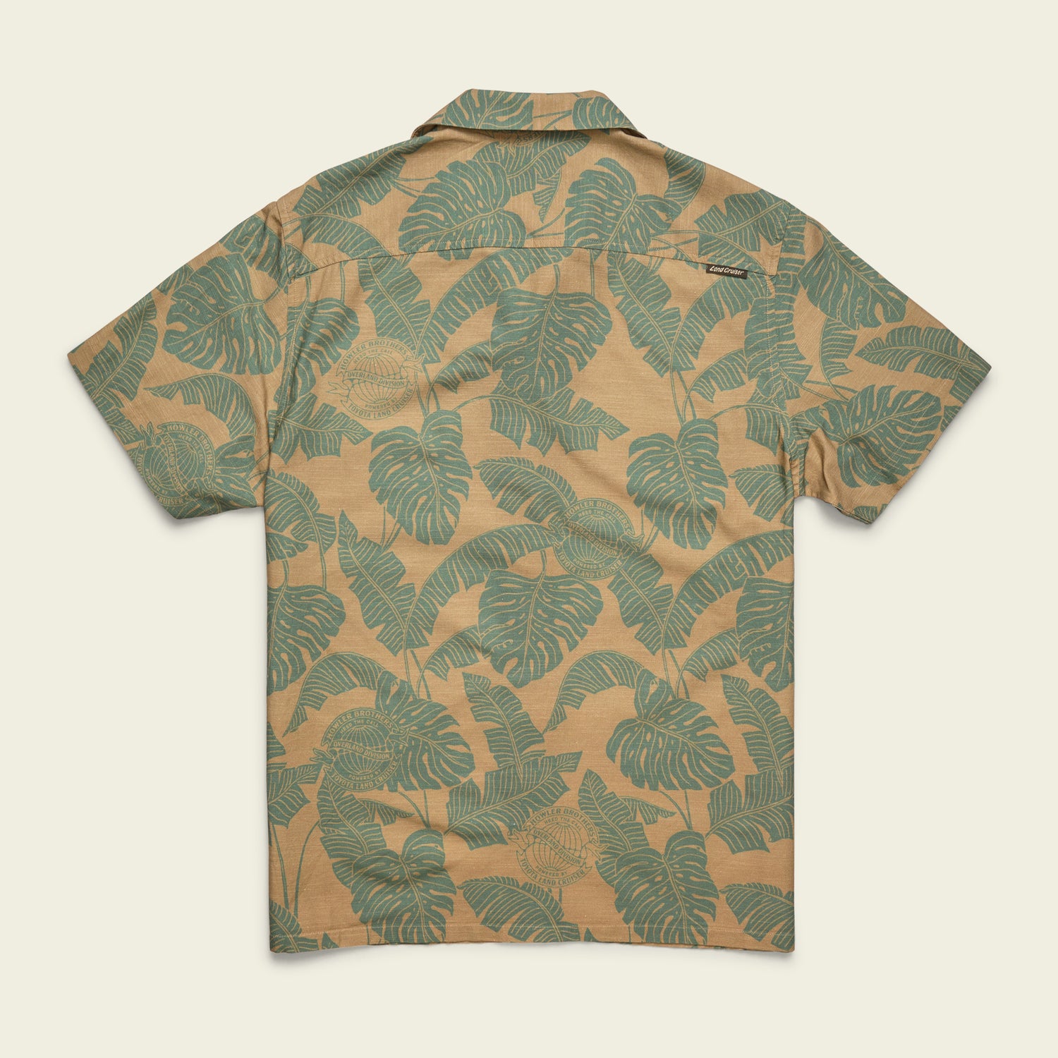 A short-sleeve button-up Monoloha Shirt with a tan background, featuring an all-over green tropical leaf print, displayed flat with the back facing up—perfect for fans of vintage Hawaiian shirts.