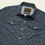 A close-up of a blue pearl snap shirt with a small floral pattern, pointed chest pockets, vented rear yoke, and a visible “Howler” brand label inside the collar.