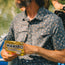 A bearded man in a pearl snap shirt holds a bag of HARIBO Goldbears gummy candy while sitting outdoors, possibly on a boat near water.