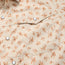 Close-up of a beige shirt with a small orange floral pattern, featuring pearl snaps, a pointed flap pocket, and crafted from durable nylon-poly fabric.
