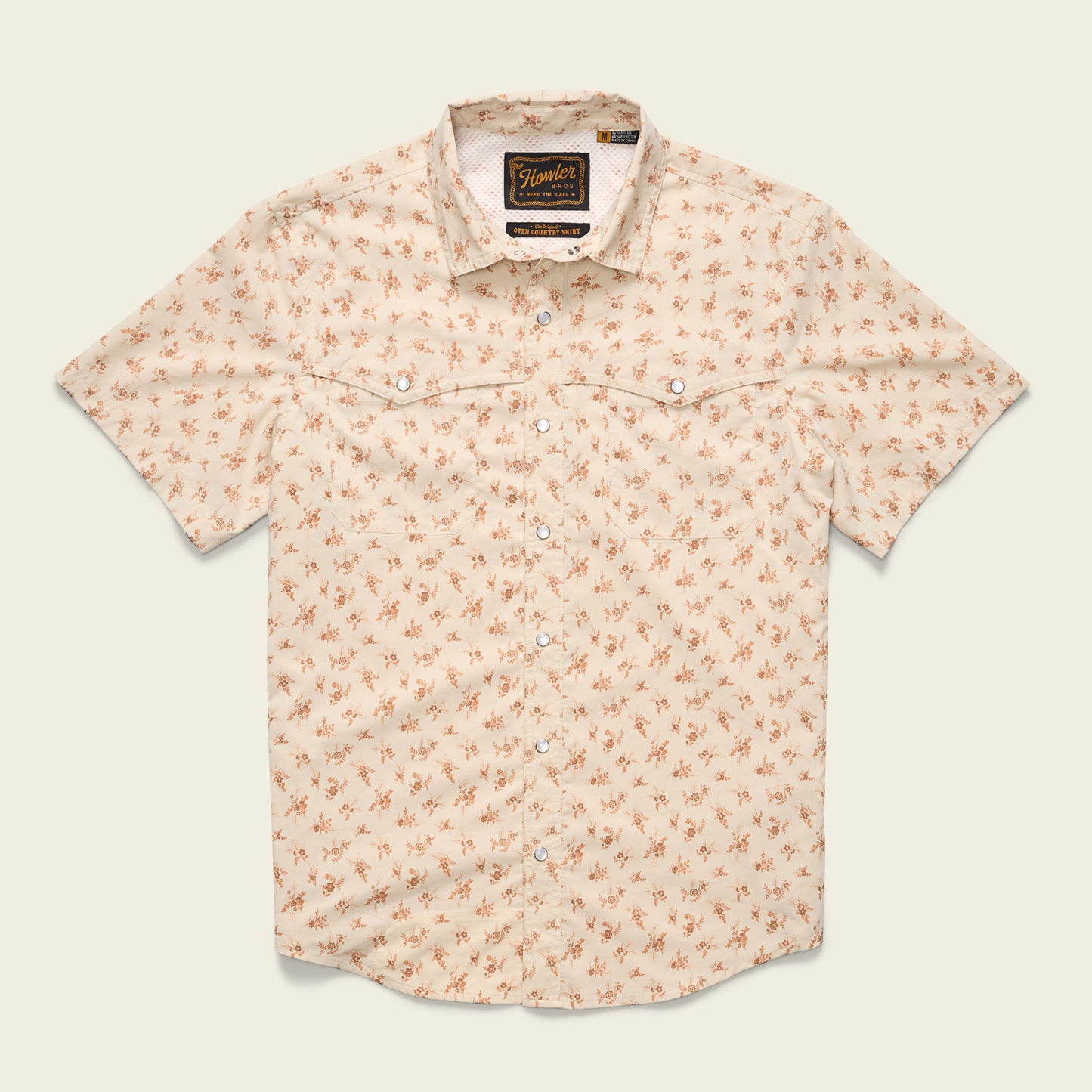 A short-sleeved, light beige button-up shirt with a small orange floral pattern, two chest pockets, pearl snaps, and a collar, crafted from nylon-poly fabric and laid flat against a plain background.