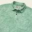 A light green textured soft polo shirt with a subtle tropical leaf pattern, button placket, and front chest pocket. The label inside the collar reads Howler Bros.