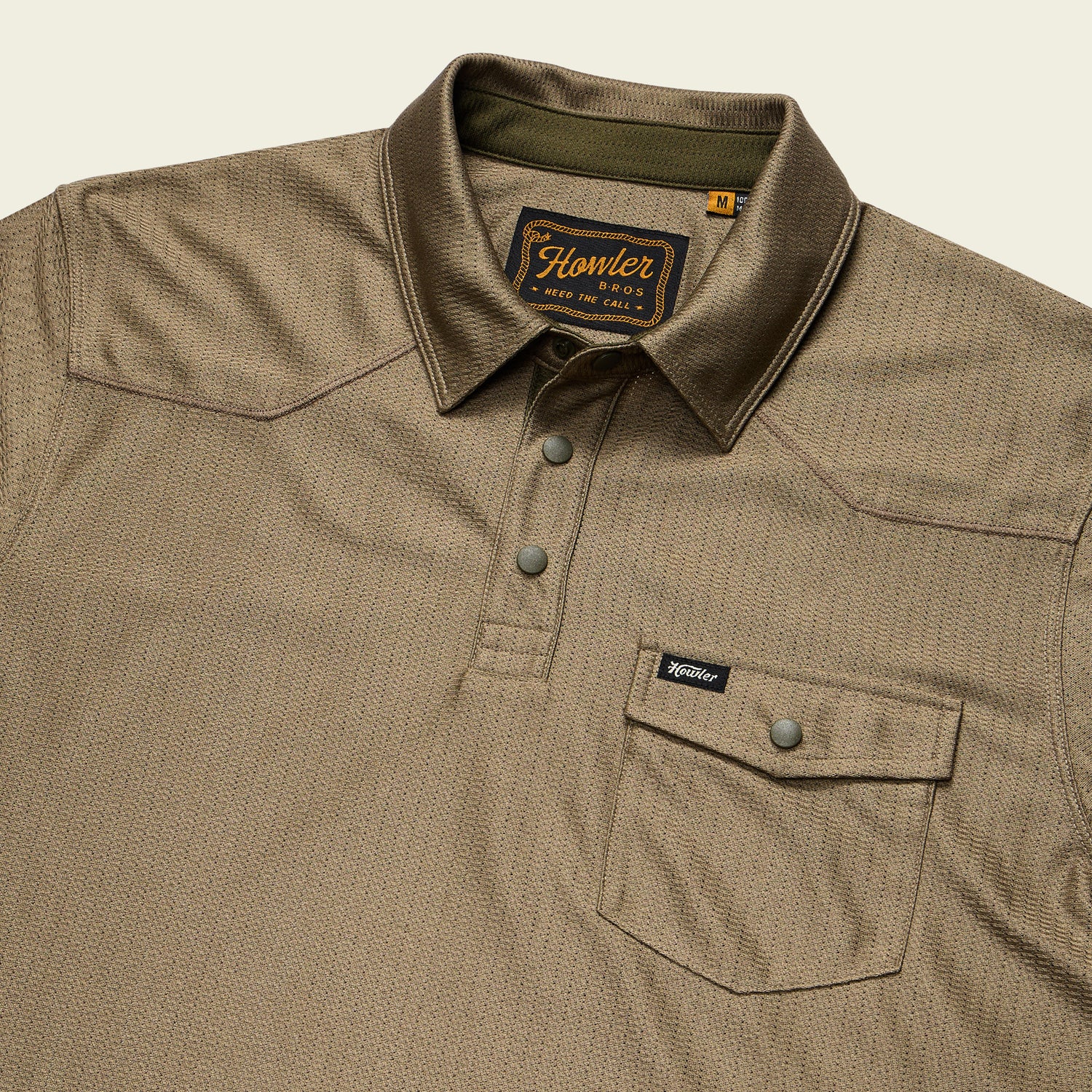 A khaki-colored tech polo with a button-up placket and buttoned chest pocket. Made from recycled polyester, it features a subtle textured pattern, Howler Bros. label inside the collar, and a small Howler tag on the pocket.