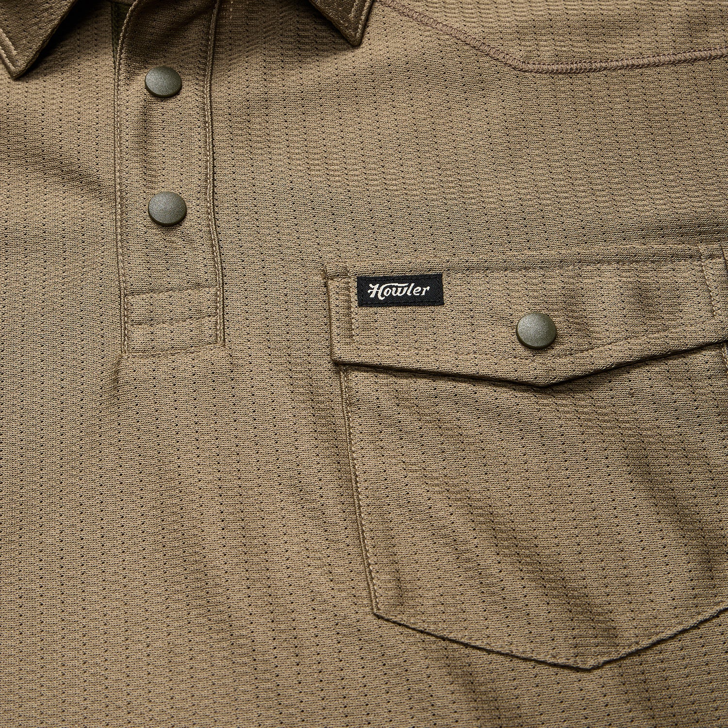 Close-up of a khaki textured shirt crafted from recycled polyester, featuring snap buttons, a flap chest pocket with a snap closure, and a small black Howler brand tag above the pocket.