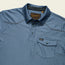A blue short-sleeve Tech Polo with three buttons, a front chest pocket with flap and button, made from breathable recycled polyester. Features the Howler Bros label on the pocket and inner collar tag.