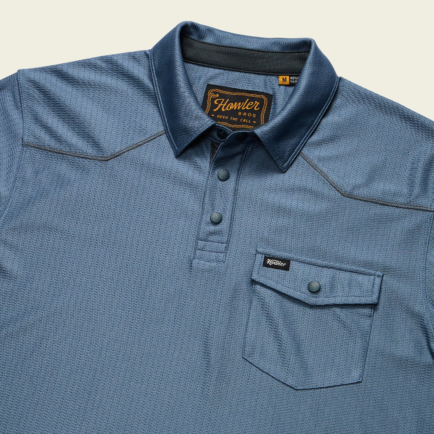 A blue short-sleeve Tech Polo with three buttons, a front chest pocket with flap and button, made from breathable recycled polyester. Features the Howler Bros label on the pocket and inner collar tag.