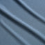 Close-up of textured blue Tech Polo fabric with small geometric patterns, featuring soft diagonal folds that create gentle shadows and highlights across the surface. Crafted from breathable recycled polyester for quick drying comfort.