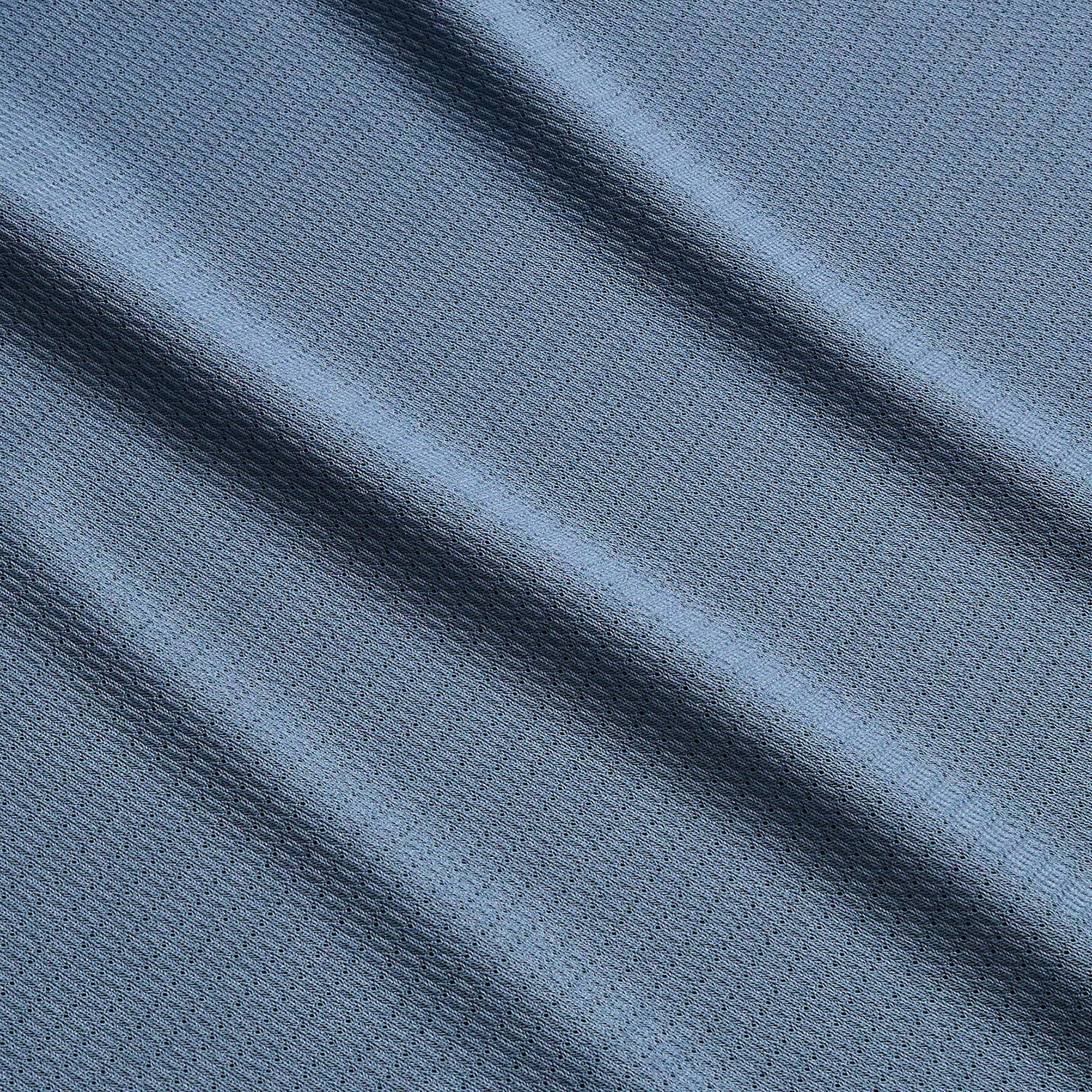 Close-up of textured blue Tech Polo fabric with small geometric patterns, featuring soft diagonal folds that create gentle shadows and highlights across the surface. Crafted from breathable recycled polyester for quick drying comfort.