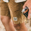 A person wearing Pressure Drop Cord Shorts, crafted from stretch cotton corduroy for comfort, holds a camera in their right hand. Only the lower torso and hand are visible.