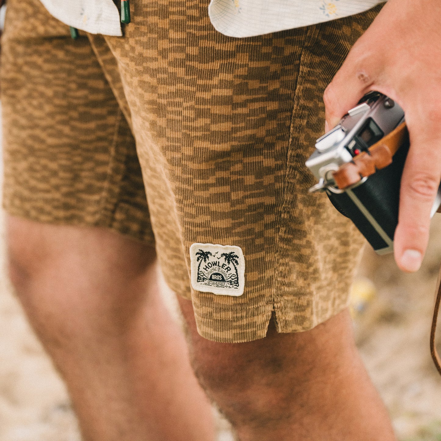 A person wearing Pressure Drop Cord Shorts, crafted from stretch cotton corduroy for comfort, holds a camera in their right hand. Only the lower torso and hand are visible.