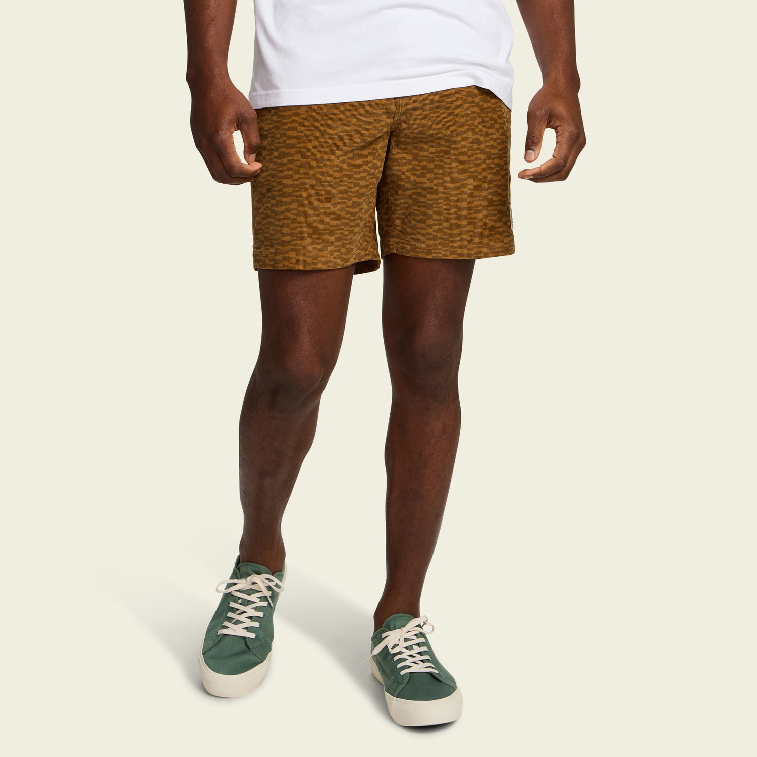 A person wearing a white shirt, Pressure Drop Cord Shorts made from stretch cotton corduroy, and green sneakers with white laces stands against a plain, light background.