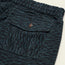 Close-up of a dark teal and black Pressure Drop Cord Shorts pocket, crafted from stretch cotton corduroy, featuring a buttoned flap, two metal eyelets, and an elastic waistband.