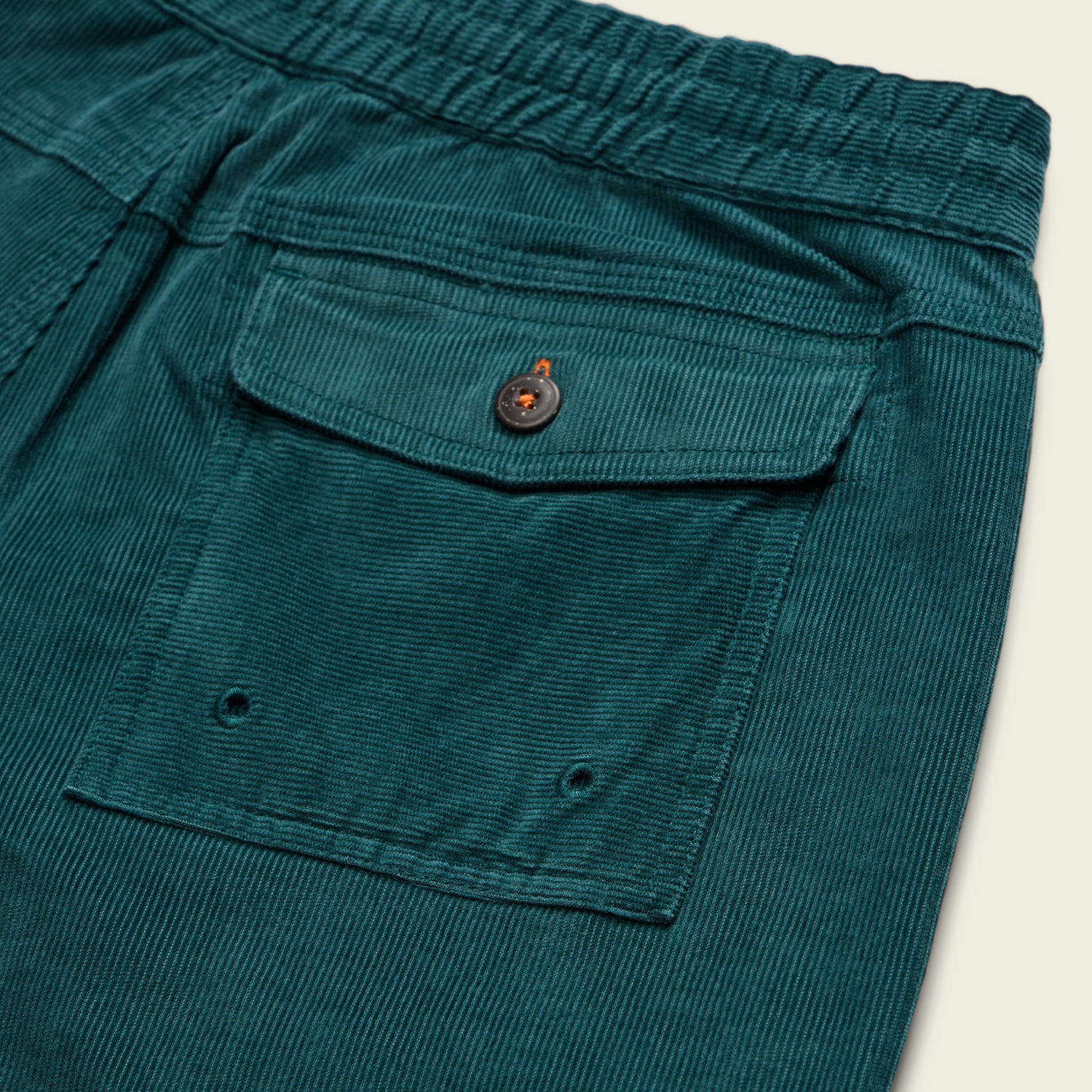 Close-up of a teal stretch cotton corduroy pocket with a flap, button closure, and elastic waistband—features seen on the Pressure Drop Cord Shorts—plus two small eyelets at the bottom for these comfortable shorts.