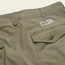 Close-up of olive green Quonset Camp Shorts crafted from ripstop cotton, featuring vintage-style buttons, belt loops, a flap pocket, and a Howler Brothers logo patch above the pocket.