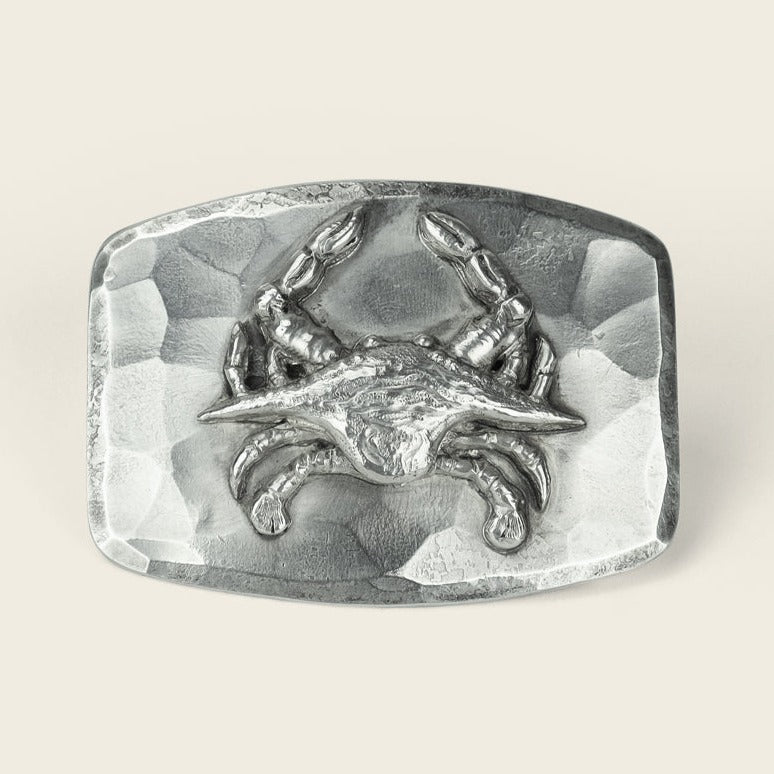 A rectangular, sterling silver buckle from Cityboy Forge features a raised, detailed crab design at its center and a hammered metal texture in the background.