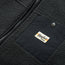 Close-up of a black high pile fleece outdoor jacket featuring a smooth black chest pocket with a snap button and a Howler BROS label. A portion of the jacket’s zipper is also visible.