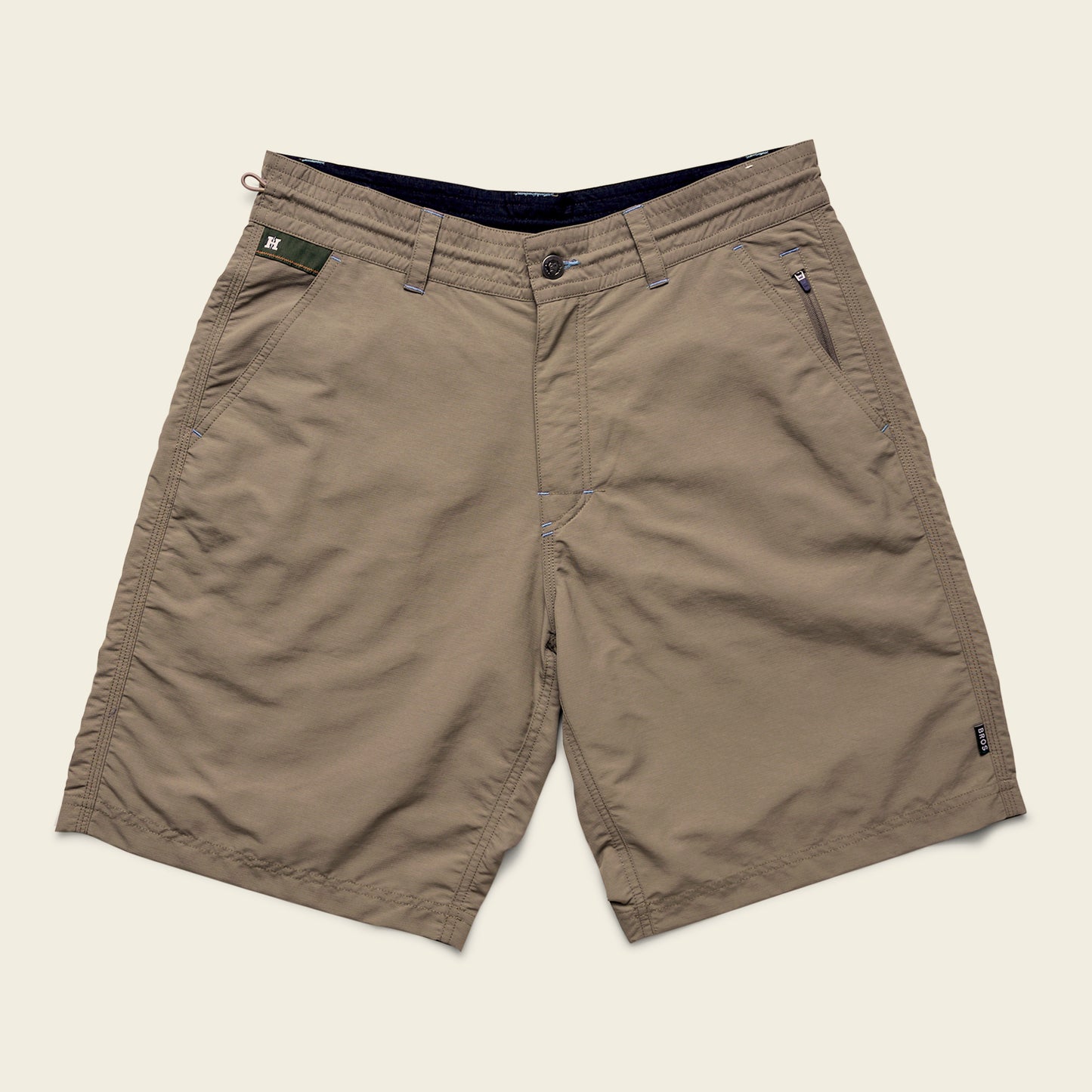 Khaki-colored Horizon Hybrid Shorts with front button and zipper closure, two side pockets, and one zippered pocket on the right. Made from durable ripstop fabric, these versatile shorts are laid flat on a light beige background.