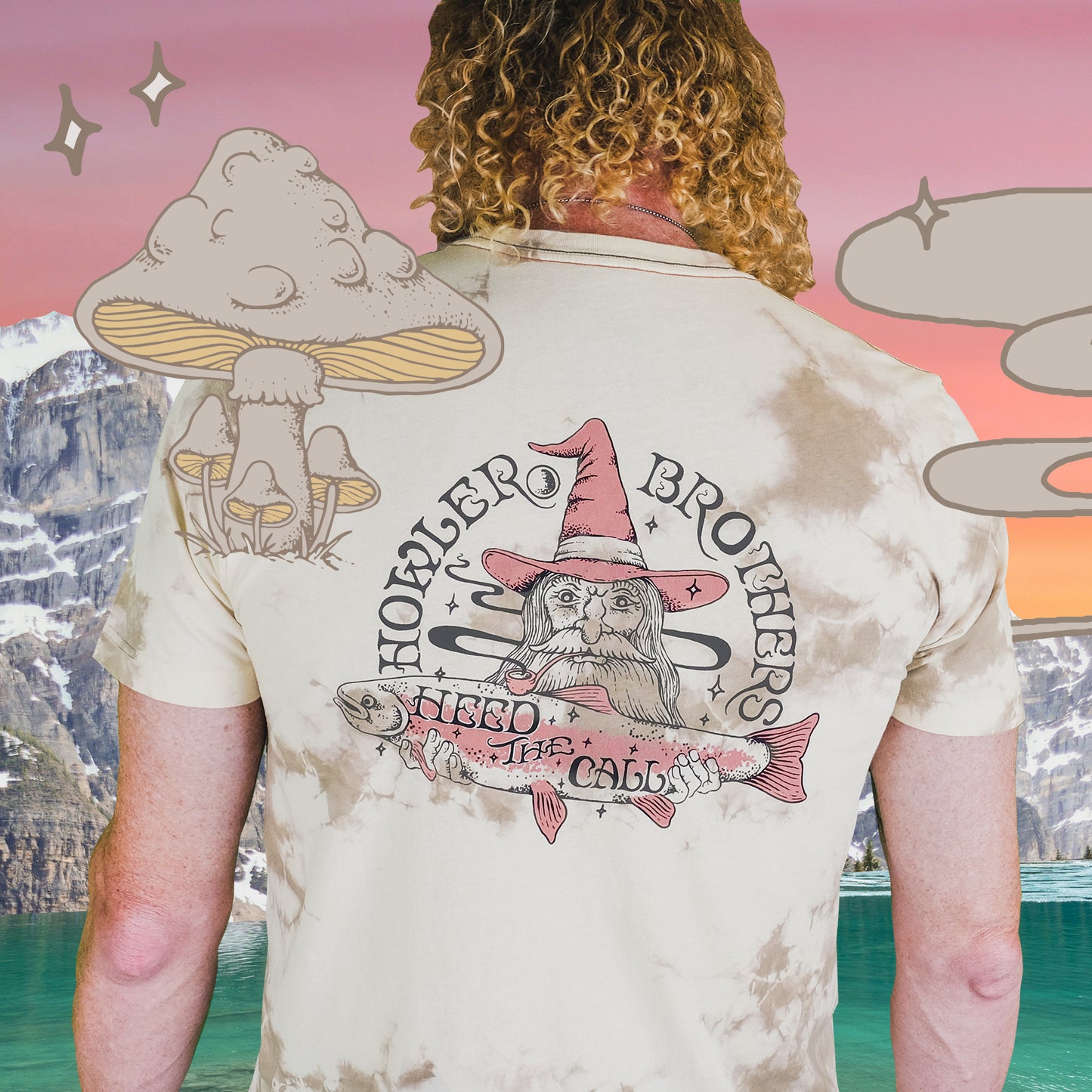 A person with curly hair faces away, wearing a tie-dye cotton t-shirt featuring a wizard holding a fish with Howler Brothers and Heed the Call text. This vintage look is accented by cartoon mushrooms, sparkles, a lake, and mountains.