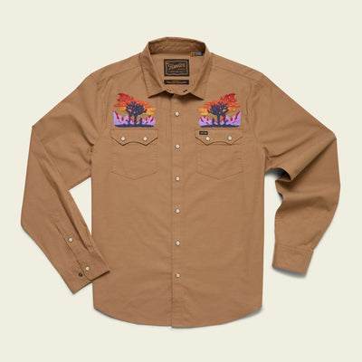 A tan long-sleeve button-up shirt crafted from stretch chambray, featuring two chest pockets and vintage inspired embroidery of sunset desert scenes with cacti and mountains on the shoulders. White buttons complete its western-style look.