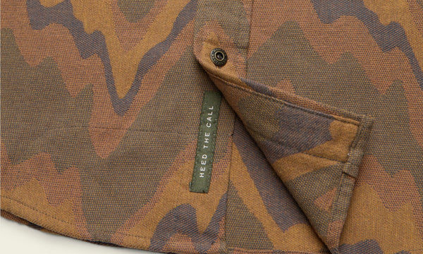 Close-up of a shirt with a brown and tan wavy, abstract pattern in buttery soft flannel. A small green tag reading HEED THE CALL is sewn on the inside hem and unbuttoned placket.