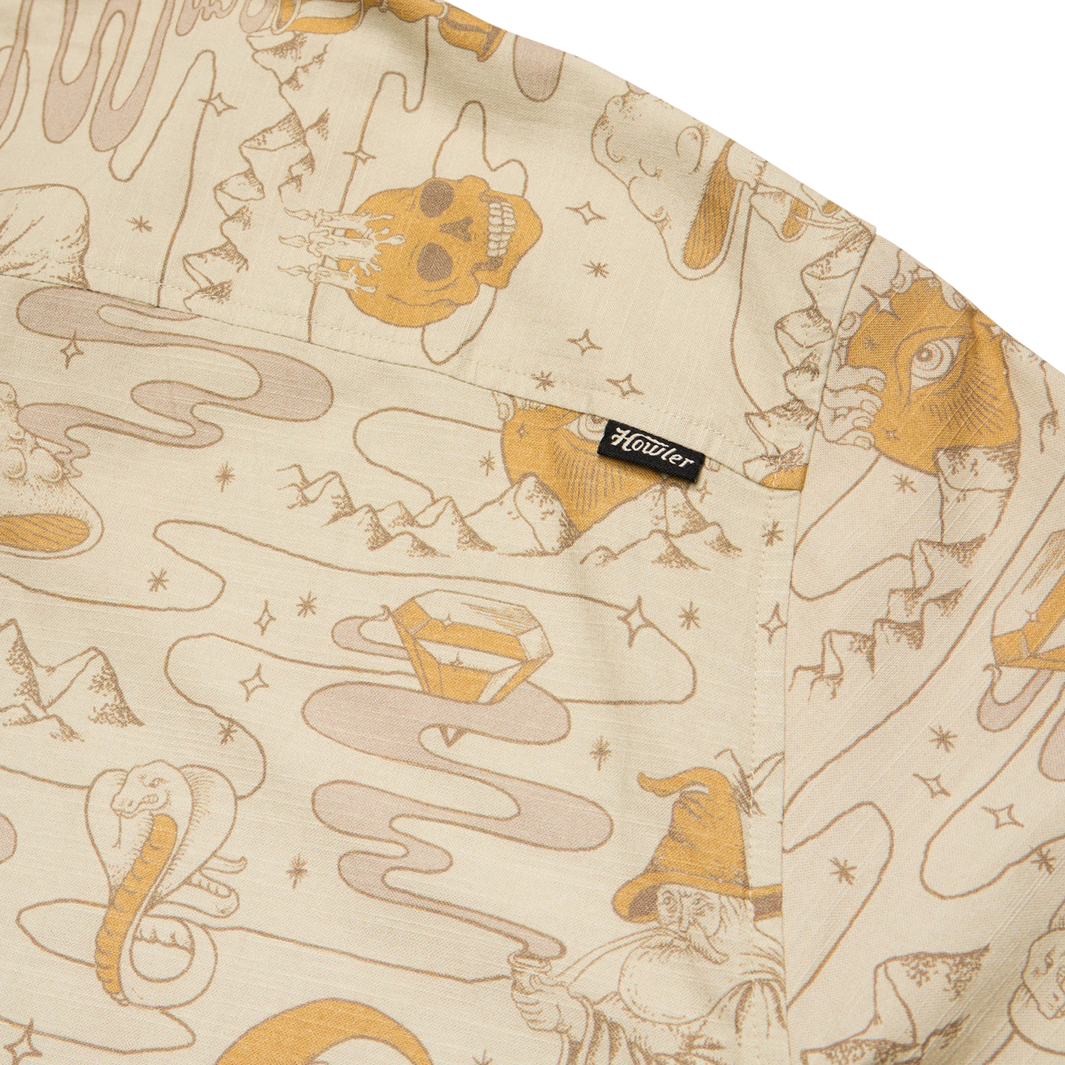 Beige slub fabric with whimsical, line-drawn illustrations including a skull, diamond, wizard, snake, all-seeing eye, and mountains—reminiscent of vintage Hawaiian shirts. A small black tag with “Houdini” is sewn onto a pocket.