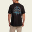 A man wearing a black cotton T-shirt with a vintage look, featuring experimental artwork of a wizard, blue star, and the text Hopper Bros and Need Chaos on the back. He stands facing away in beige pants.