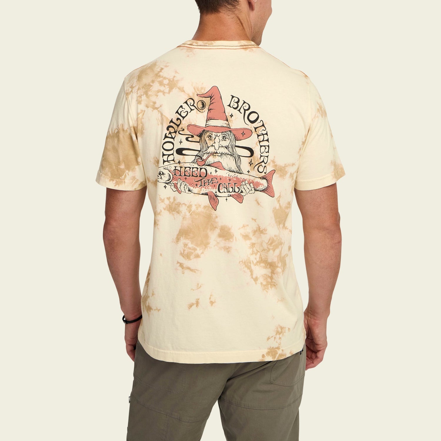 A man wearing a vintage look tan tie-dye cotton T-shirt with a graphic on the back featuring a wizard in a pink hat, text that reads Howler Brothers, and a banner that says Hero of the Chillness.