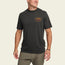 A man wearing a black short-sleeve t-shirt made from a soft cotton-poly blend with an orange Outdoor Research logo on the left chest, paired with olive green pants, stands against a plain light background and smiles while looking to the side.