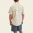A man stands facing away, wearing a lightweight cotton shirt with a single pocket and blue shorts against a plain, light background.