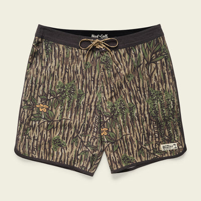 A pair of Bruja Boardshorts with a tree bark and leaves camouflage pattern, featuring stretchy fabric, a black waistband, brown drawstring, draining front pockets, and a small white Howler label near the bottom hem.