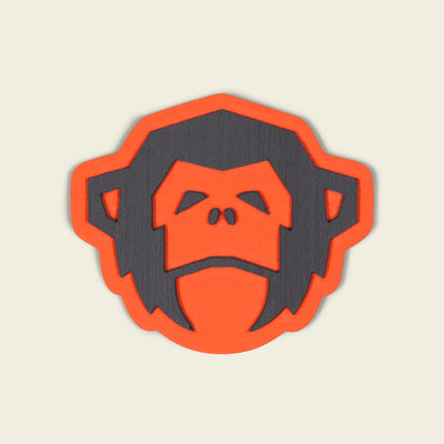 A stylized, flat illustration of a chimpanzee’s face in dark gray with an orange outline and background, set against an off-white backdrop, inspired by the resilience of industrial-strength adhesive.